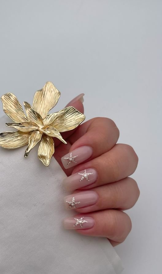 Almond nails in soft nude with a gold flower ring